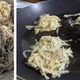 on the left, shredded potatoes with skin on in a bowl. on the right, latke mix in formed latkes frying in a shallow pan of oil.